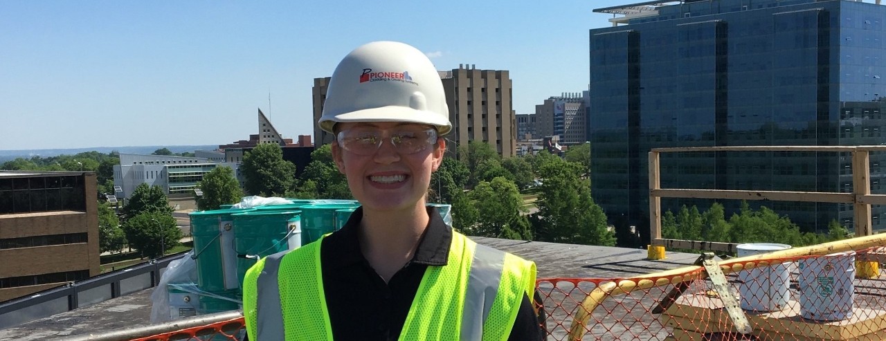 young woman wearing a hard hat, safety goggles and safety vest on the roof of a building on the University of Cincinnati Clifton campus
