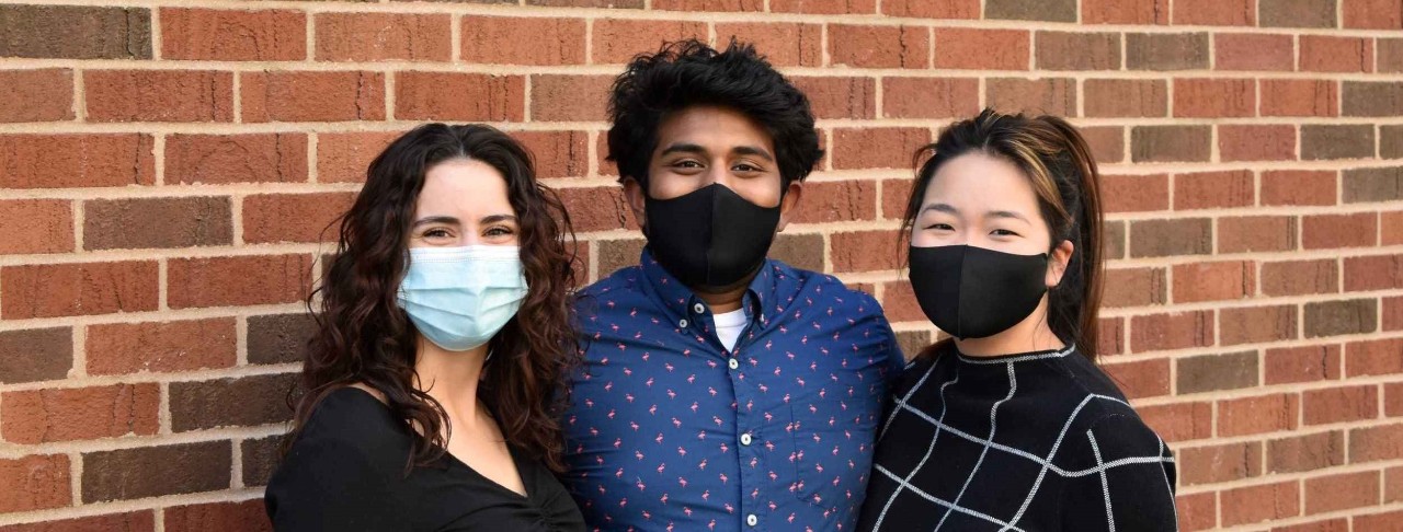 two young women and a young man wearing masks pose together