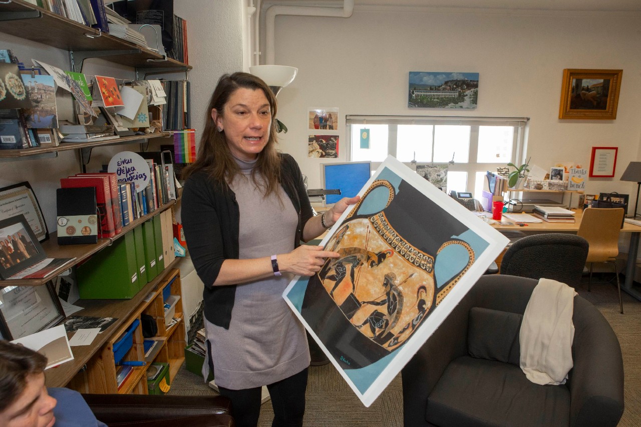 UC Classics professor Kathleen Lynch holds up a painting of an ancient vase in her office.