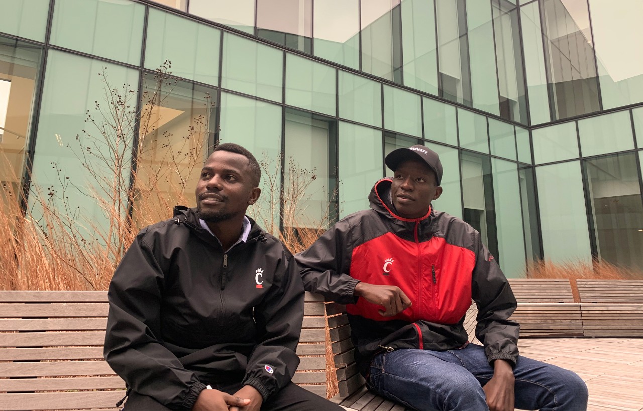 Two students from Tanzania sitting outside wearing UC gear