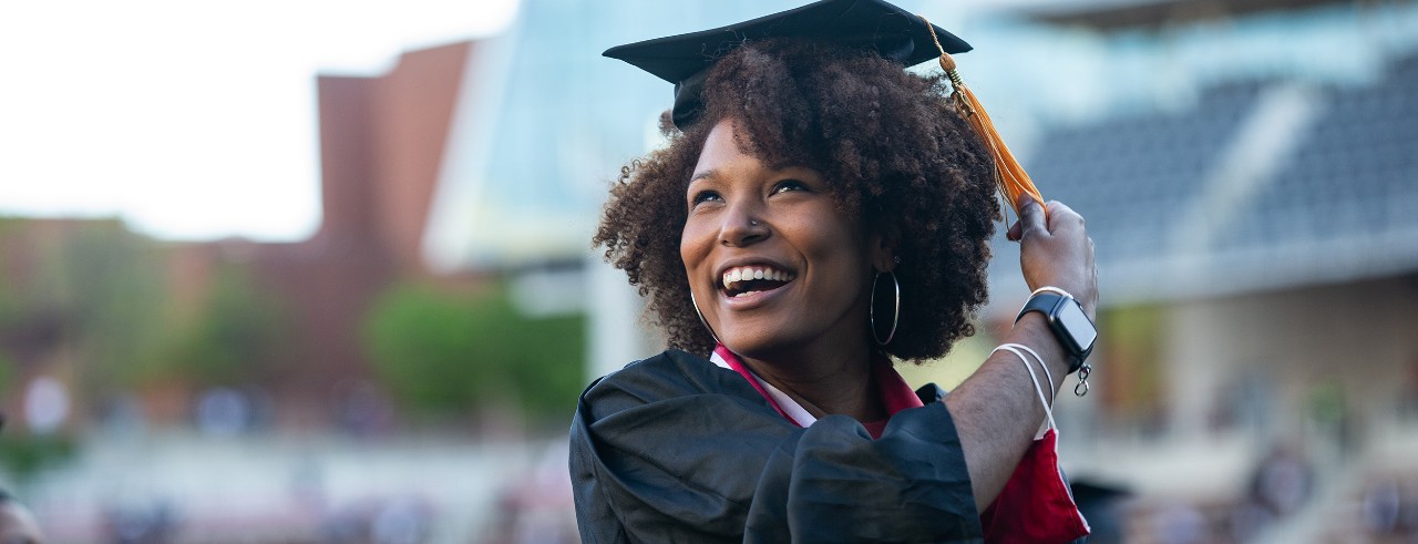 A UC student smiles in her cap and gown as she turns her tassel to mark her commencement.