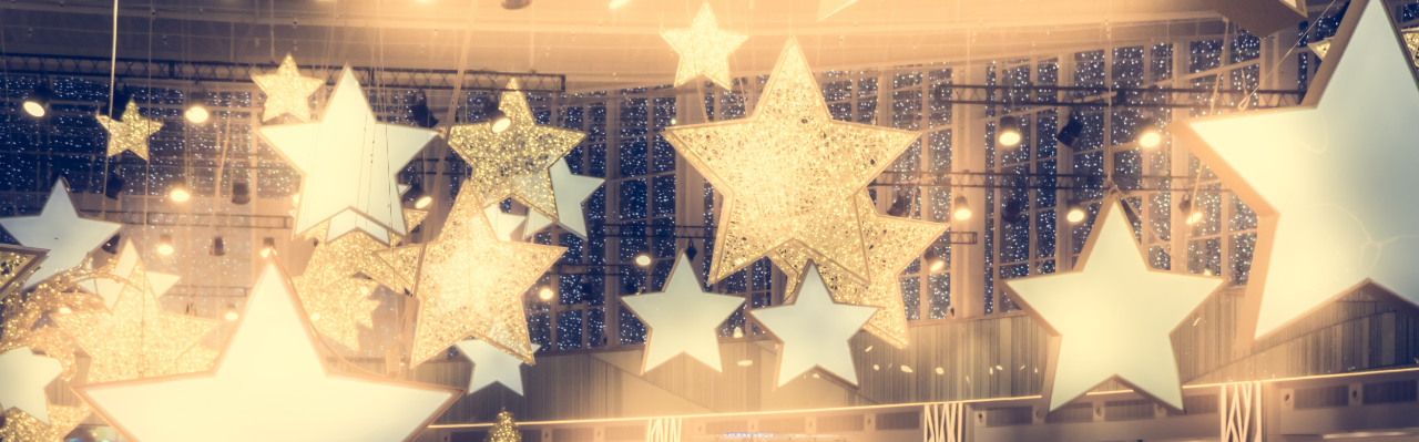 glittery glowing golden star shaped lights hanging from the ceiling of a room with high windows in the background