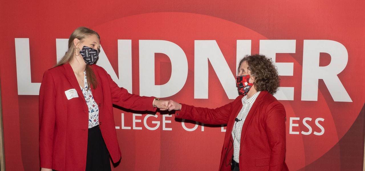 two women in red blazers and white blouses fist bump in front of a red LINDNER banner