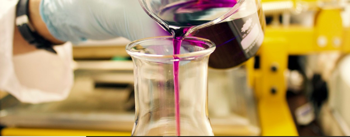 hand pouring purple liquid from one beaker to another in a lab