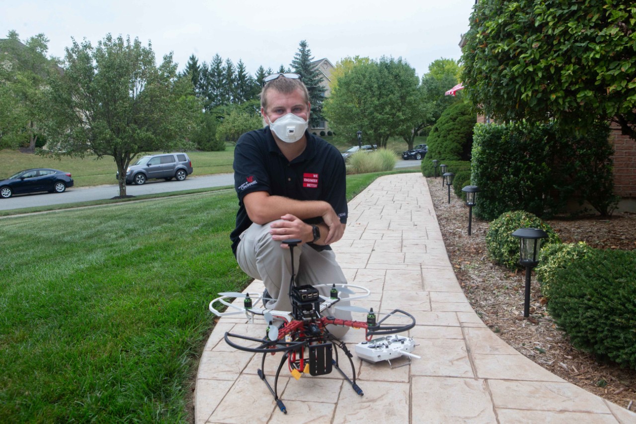 A UC student kneels next to a drone.