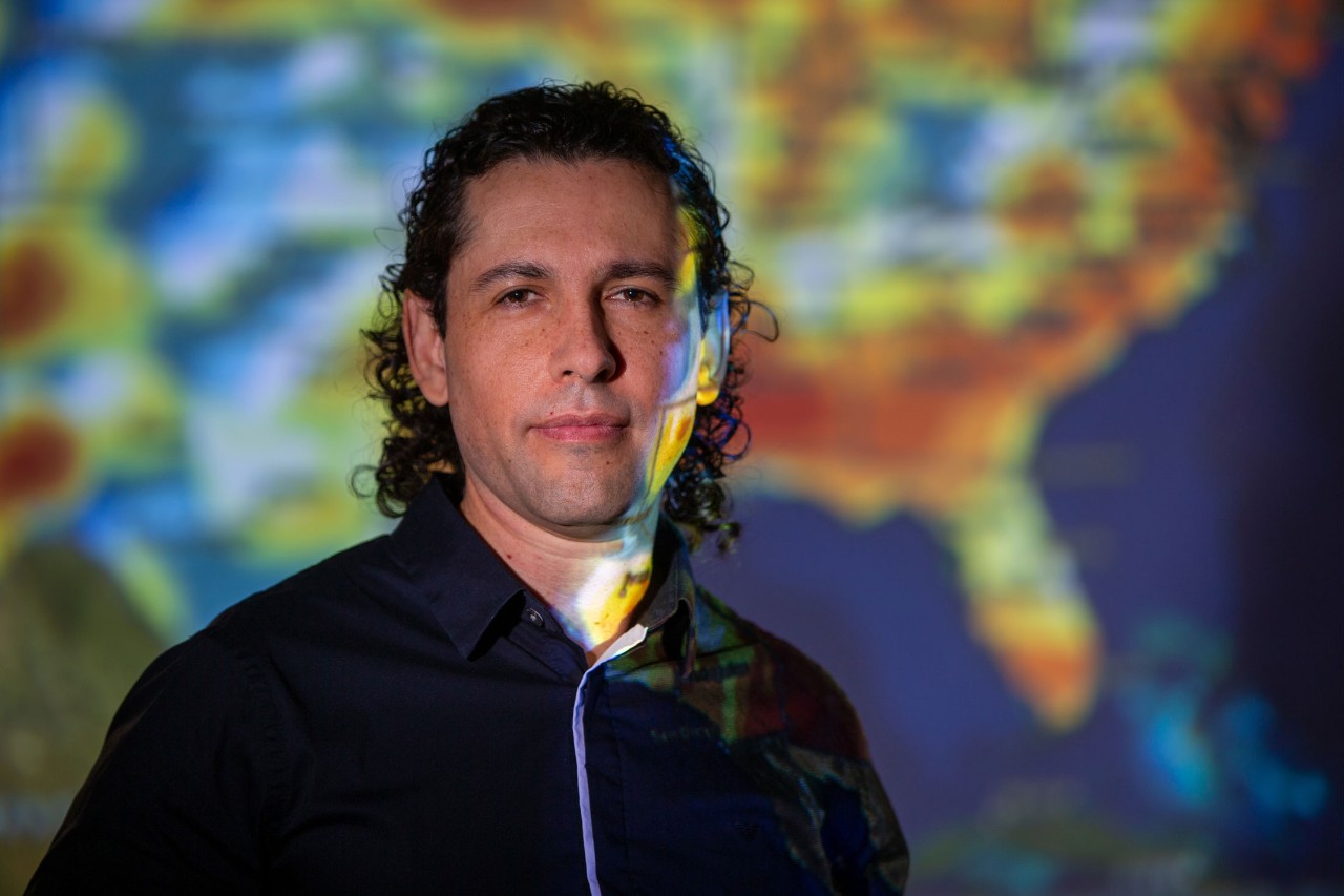 Diego Cuadros stands in front of a colorful projected map of America.