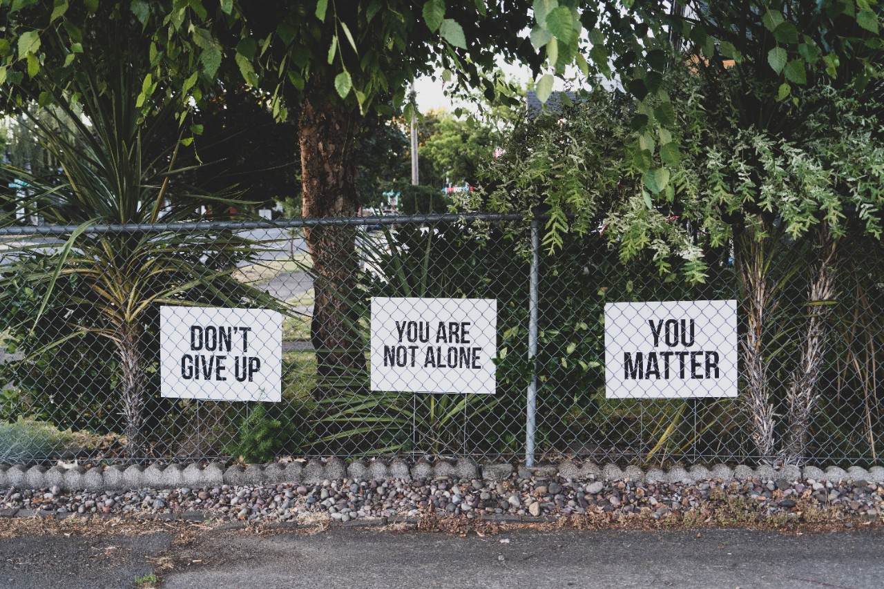 Three signs on a chain-link fence read dont give up, you are not alone and you matter.