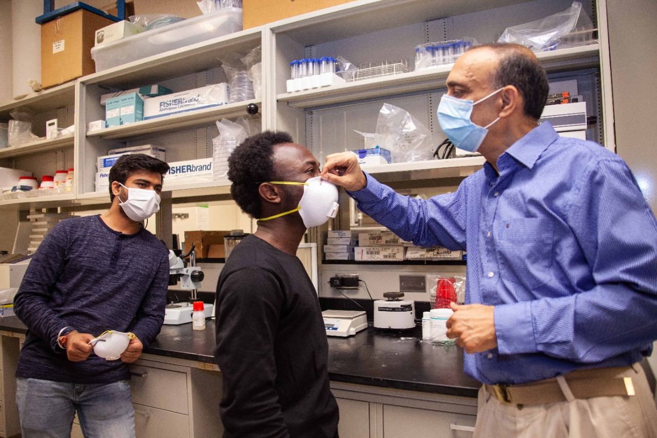 Professor Rupak Banerjee adjusts a face mask of a student model in his lab while another student looks on.