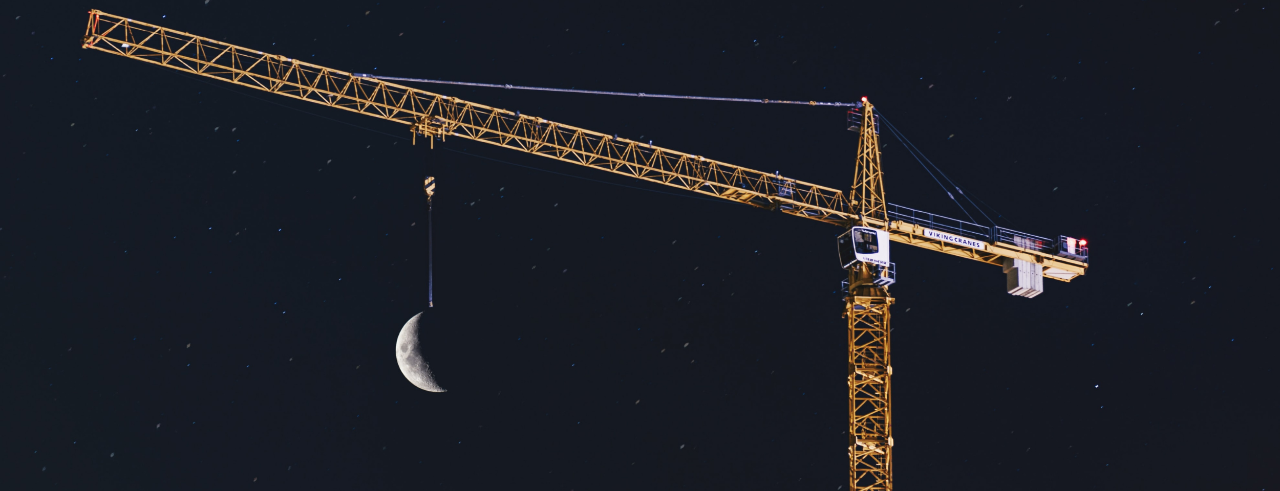 A yellow construction crane against the night sky, the moon appearing to hang from its chain