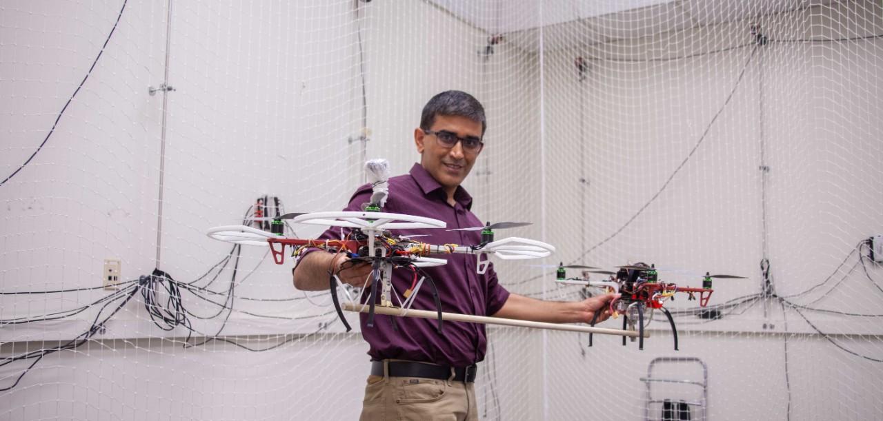 Manish Kumar holds up two drones in his lab.