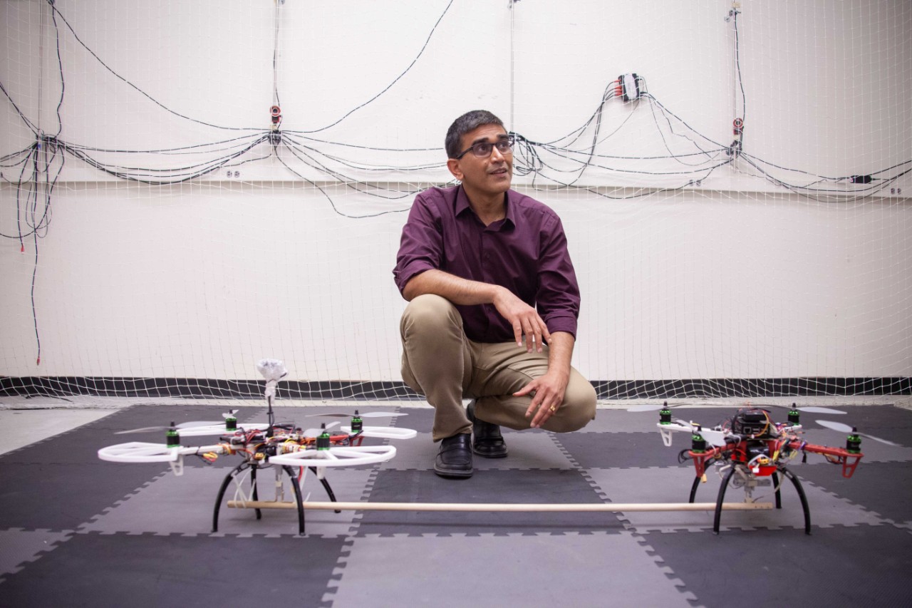 Manish Kumar kneels in front of twin drones in his flight cage.