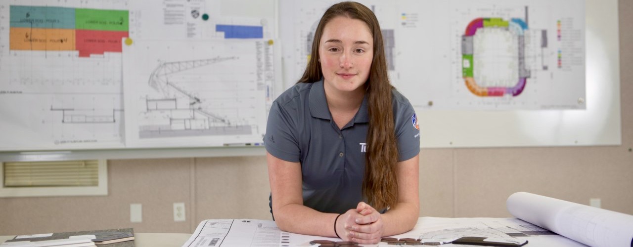 UC women co-op student leans on blueprints spread across a table.