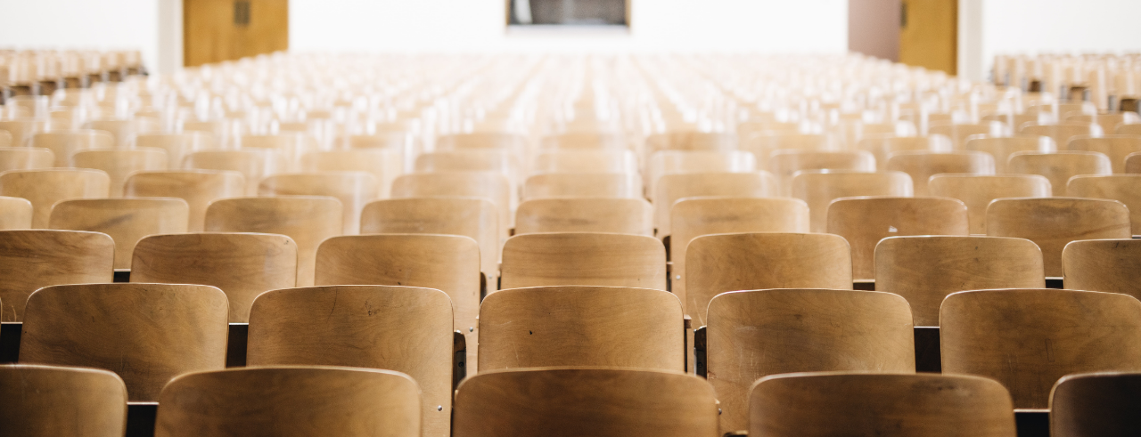 rows of wooden chairs in an auditorium, looking at the back of the room