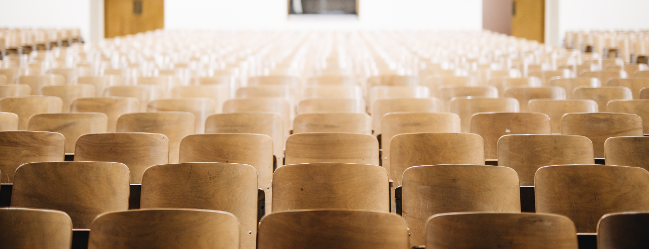 rows of wooden chairs in  an auditorium, looking at the back of the room