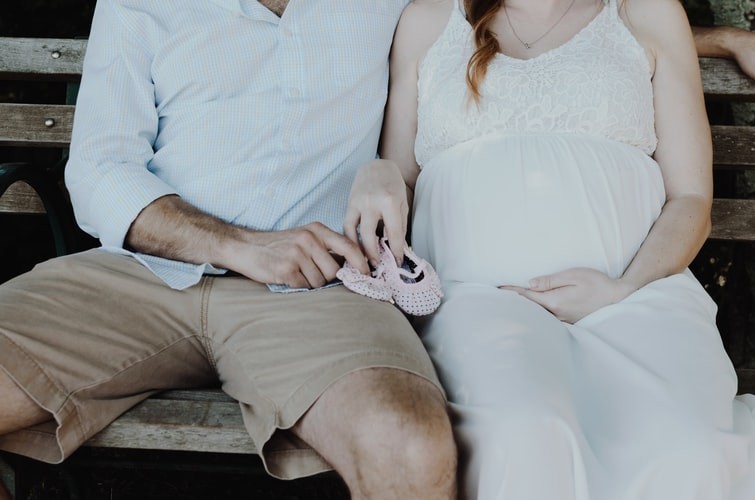 Male-female couple expecting a baby sitting and holding baby shoes.