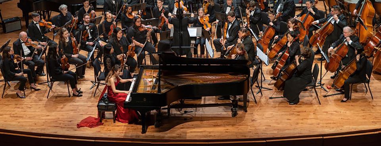 A pianist performing with an orchestra on stage