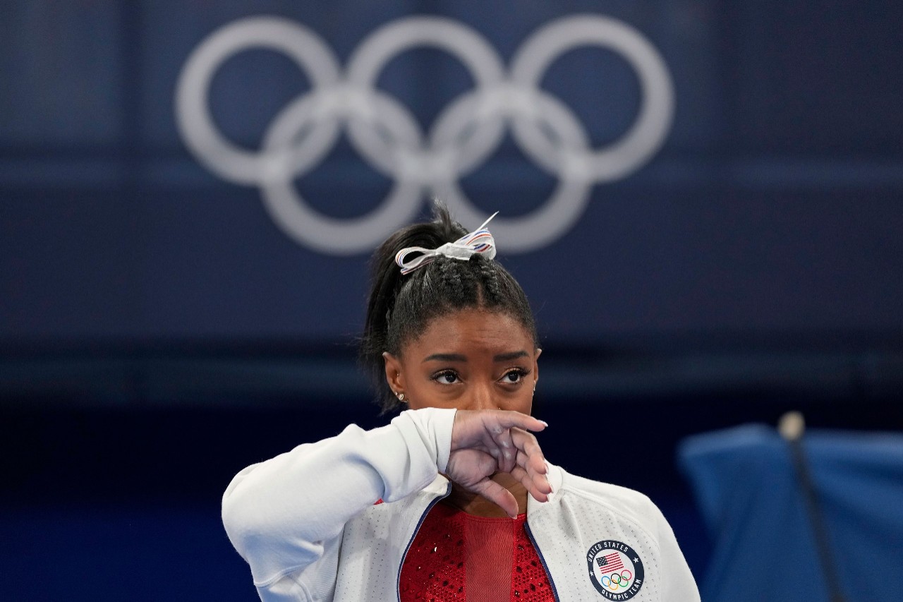 gymnast simone biles standing in front of the olympic rings