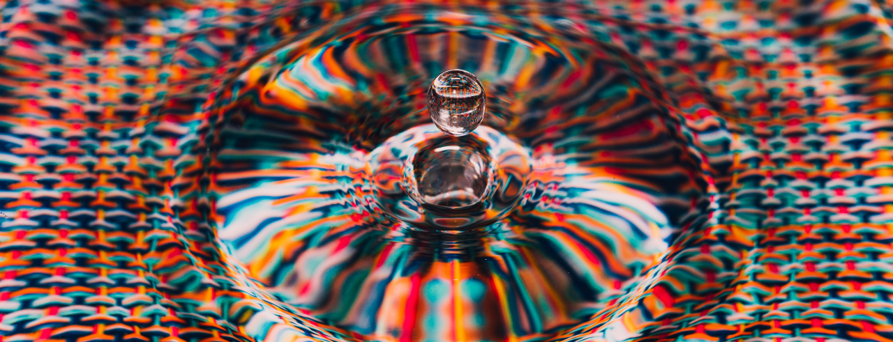 a water droplet floating in the air above water with a colorful background under it