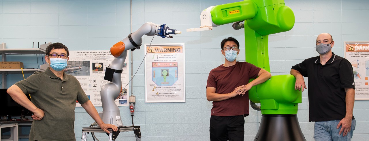 Ou Ma, Yufeng Sun and Andrew Barth pose in face masks in front of two robotic arms in an engineering lab.