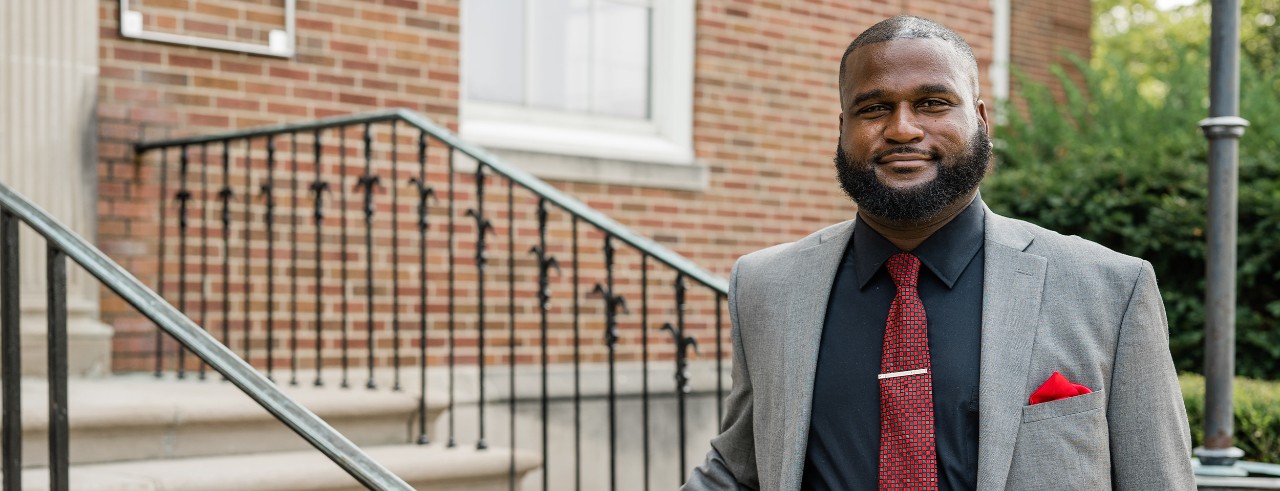 Damon Davis wearing gray jacket, red tie in front of University of Cincinnati building