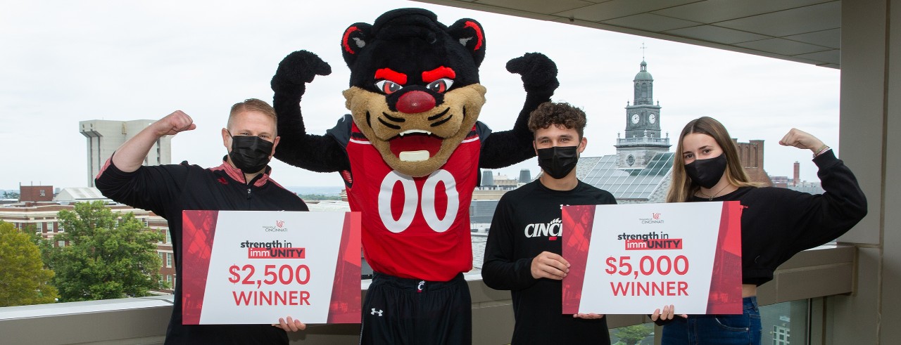 Three people in masks pose with Bearcat mascot