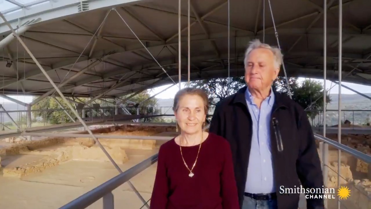 A still frame of the show "Secrets" shows Sharon Stocker and Jack Davis giving a tour of the excavation site.