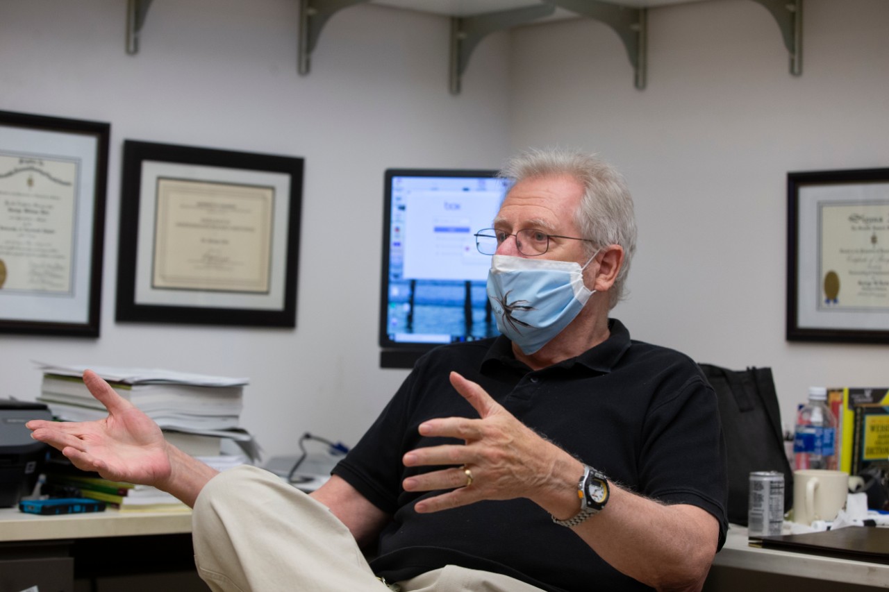 George Uetz wearing a face mask with a spider on the front talks in his office.