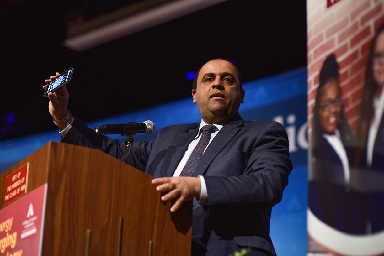 Hazem Said holds up a cell phone at a podium while giving a talk.