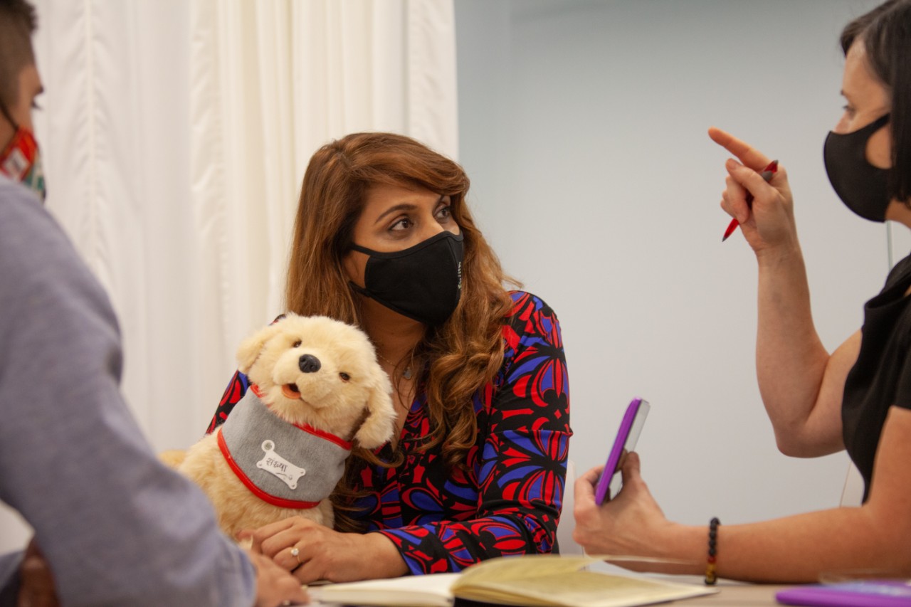 Woman holding robot puppy talks with two researchers