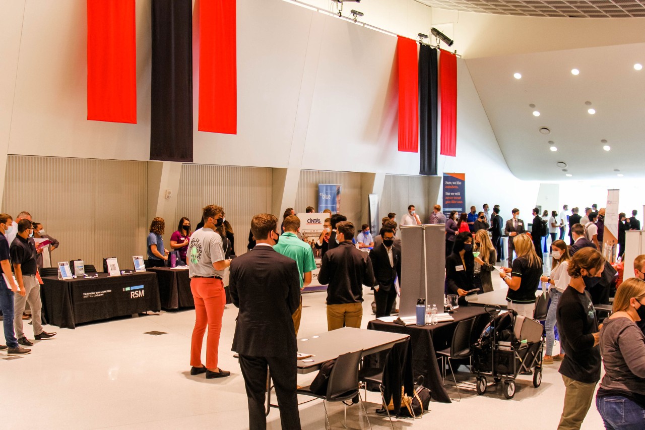 Photo of dozens of individuals in large hall with red and black banners and set up like an exhibit