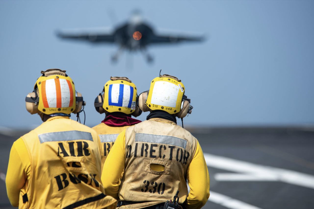 U.S. Navy personnel wear hearing protection aboard an aircraft carrier.