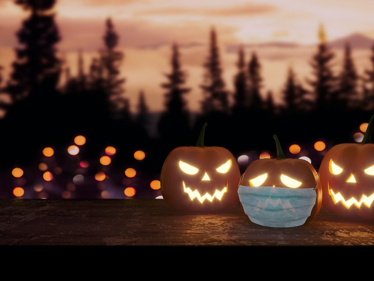 a photo at dusk showing lit carved halloween pumpkins with one wearing a surgical mask
