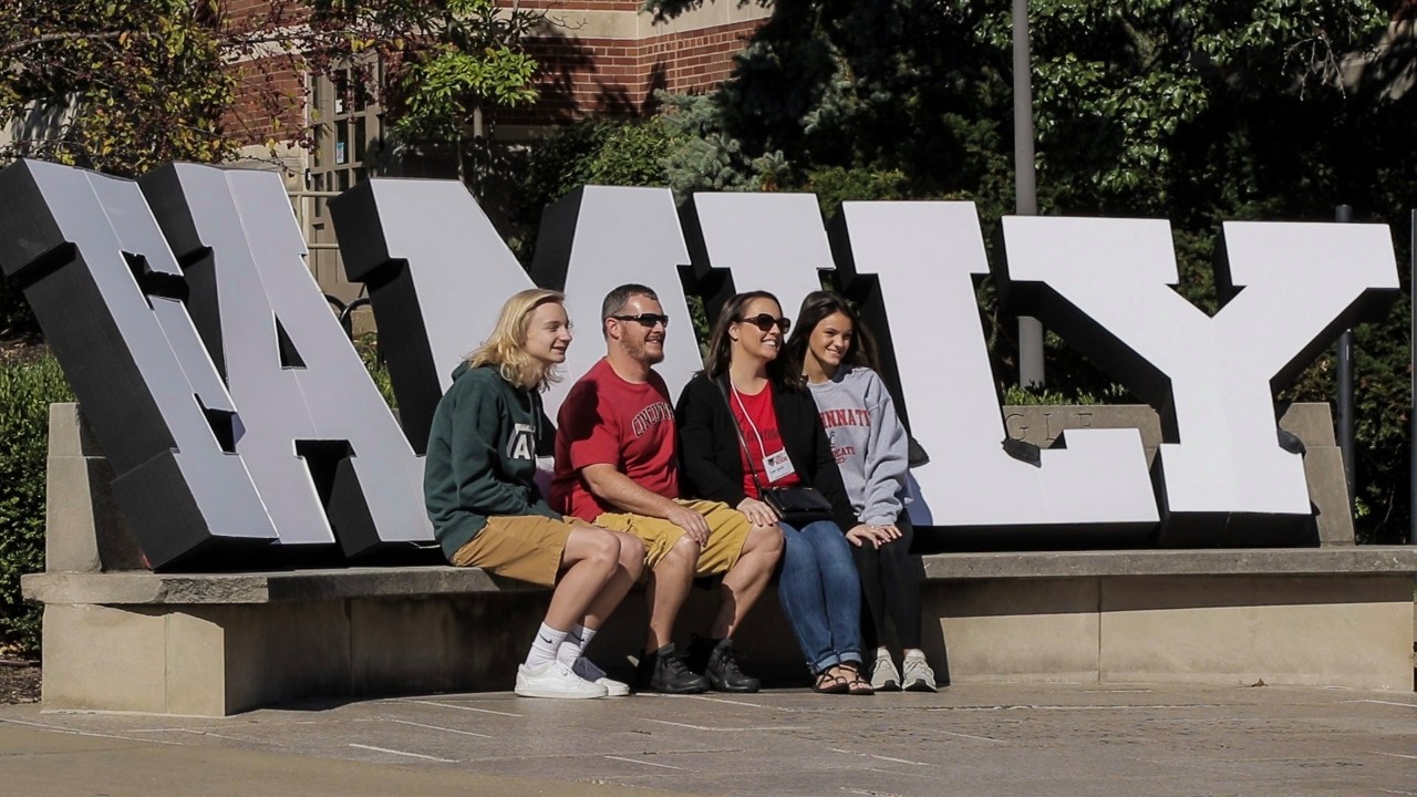 family members seated in front of a sign reading family on the UC campus