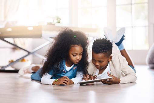 kids lying on the floor looking at a tablet