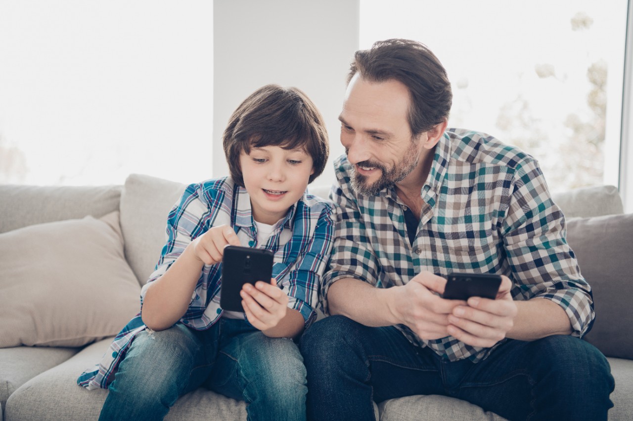 A sitting child holds a mobile phone for a sitting adult to see.