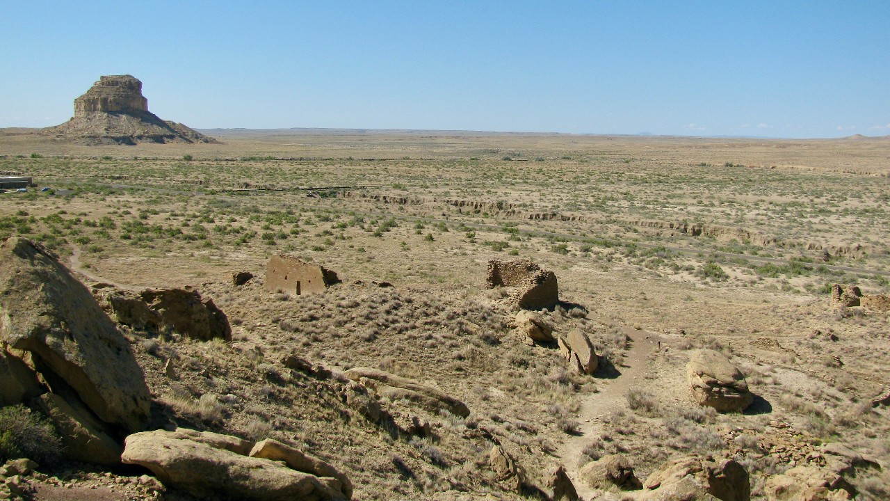 The rocky remains of Fajada Butte in background with the largest ancient great house in foreground in Chaco Canyon, New Mexico desert.