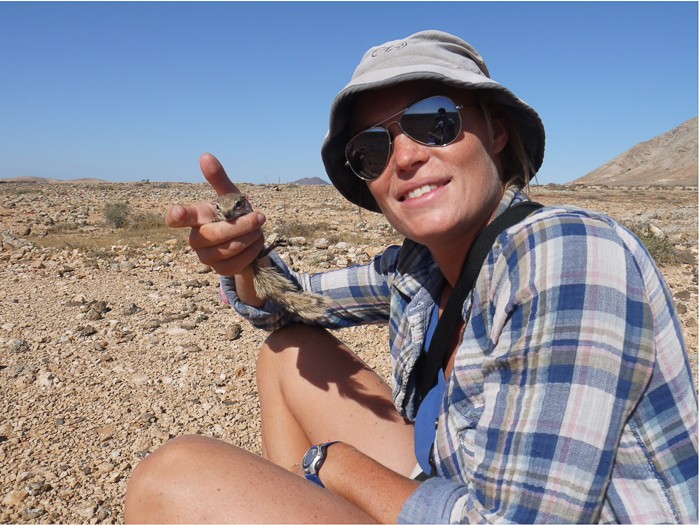 UC postdoctoral researcher Annemarie van der Marel wearing a sun hat and sunglasses holds a Barbary ground squirrel in the arid, rocky landscape of the Canary Islands..