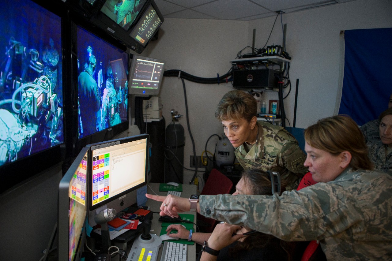 two women in military uniforms look at a computer monitor in a medical simulator