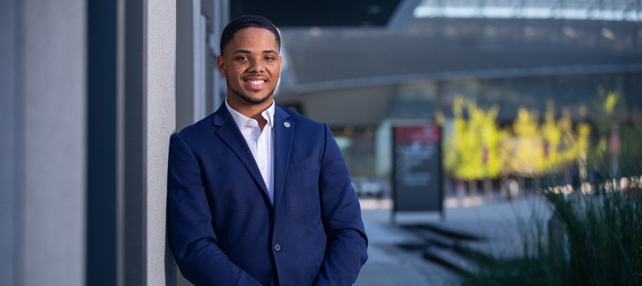 First generation college student Donald Whittle in a suit leaning up against a wall on campus