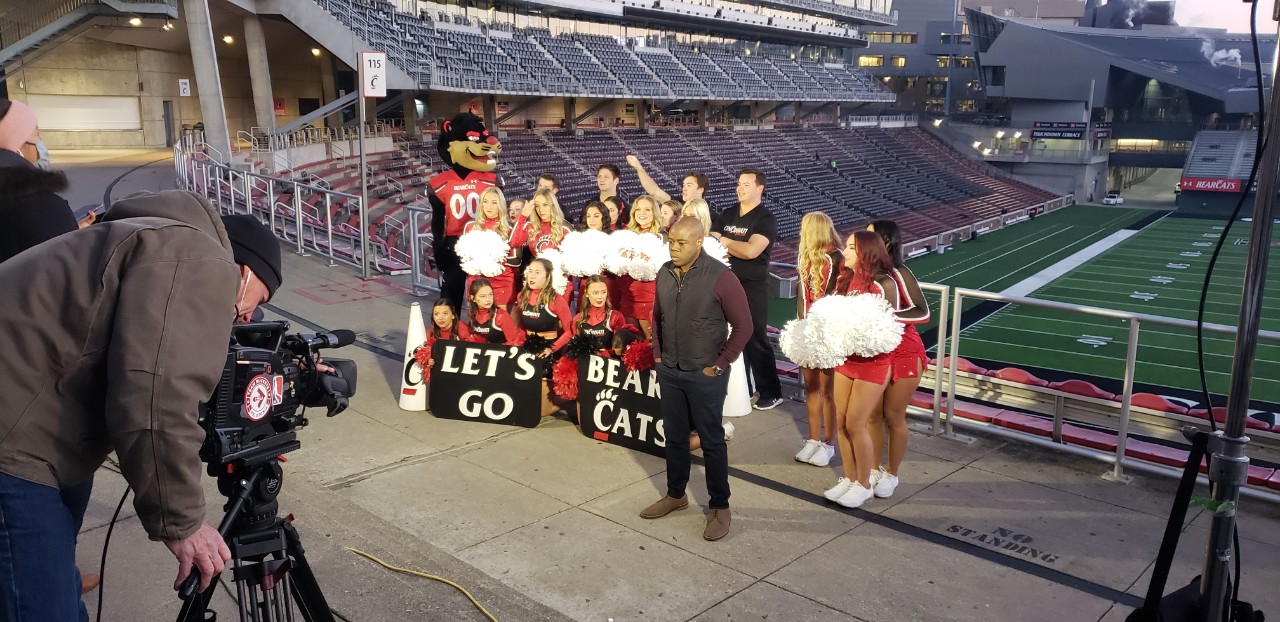 UC dance and cheer team shown in front of Nippert Stadium with Good Morning American correspondent in front.  Cameramen tapes.