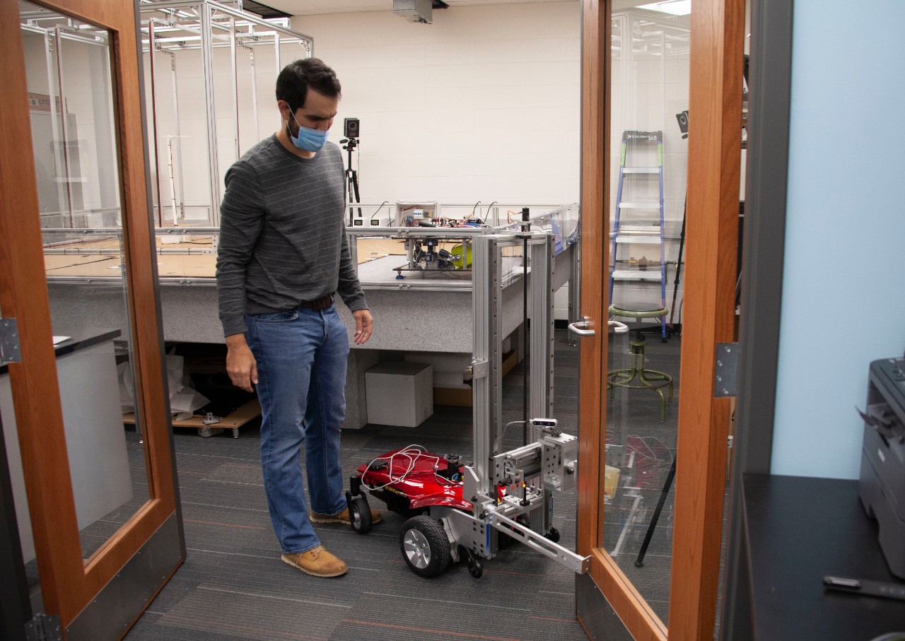 A student in a face mask stands nest to a robot holding open a door.