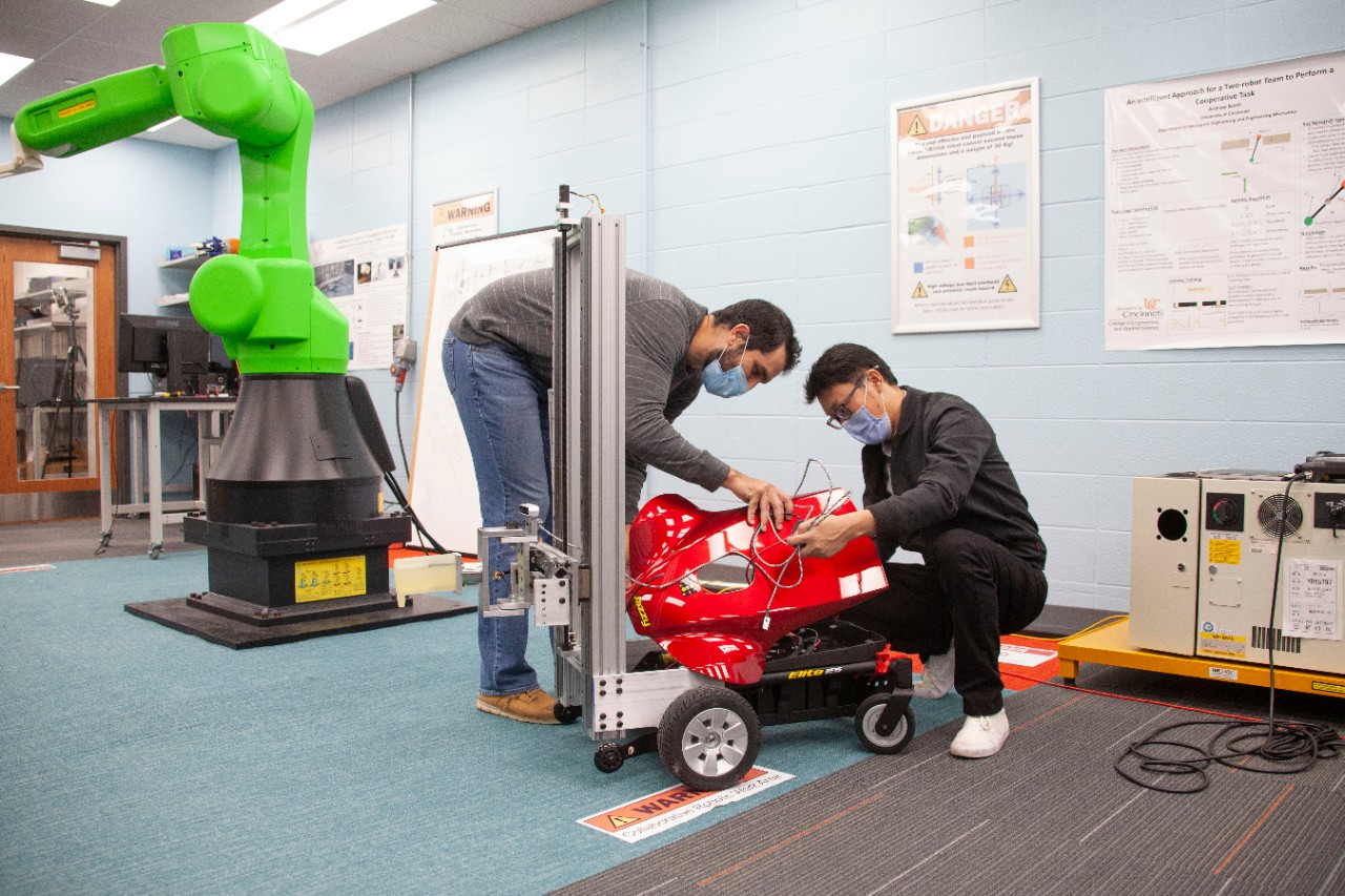 Sam King and Yufeng Sun stand next to their autonomous robot in a robotics lab.