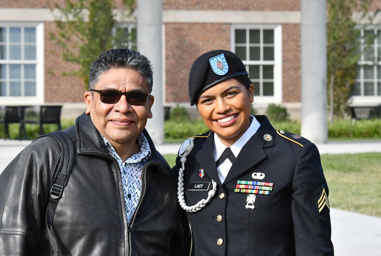 A UC student in uniform poses for a photo with her dad on UC's McMicken Commons.