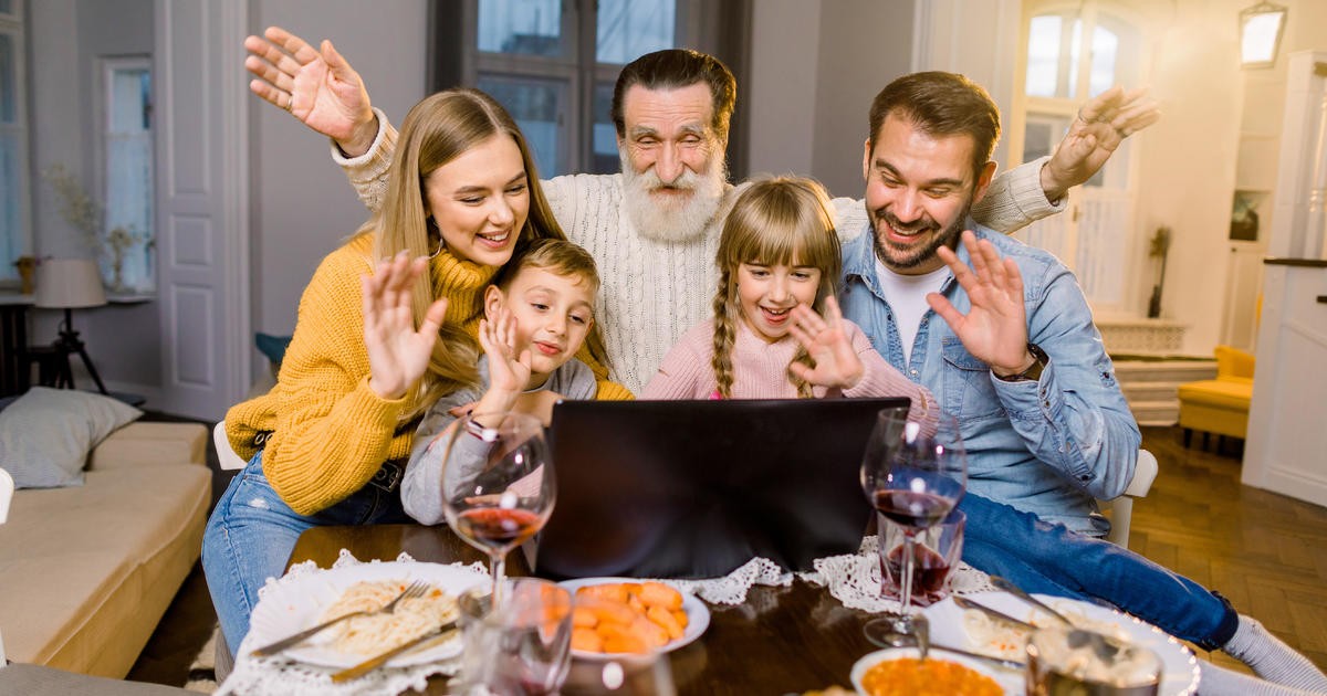 A family celebrating Thanksgiving virtually by waving at a group on a laptop