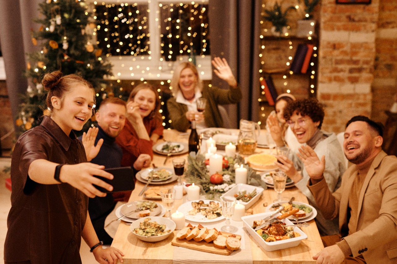 a woman takes a selfie of a holiday gathering around a dining table