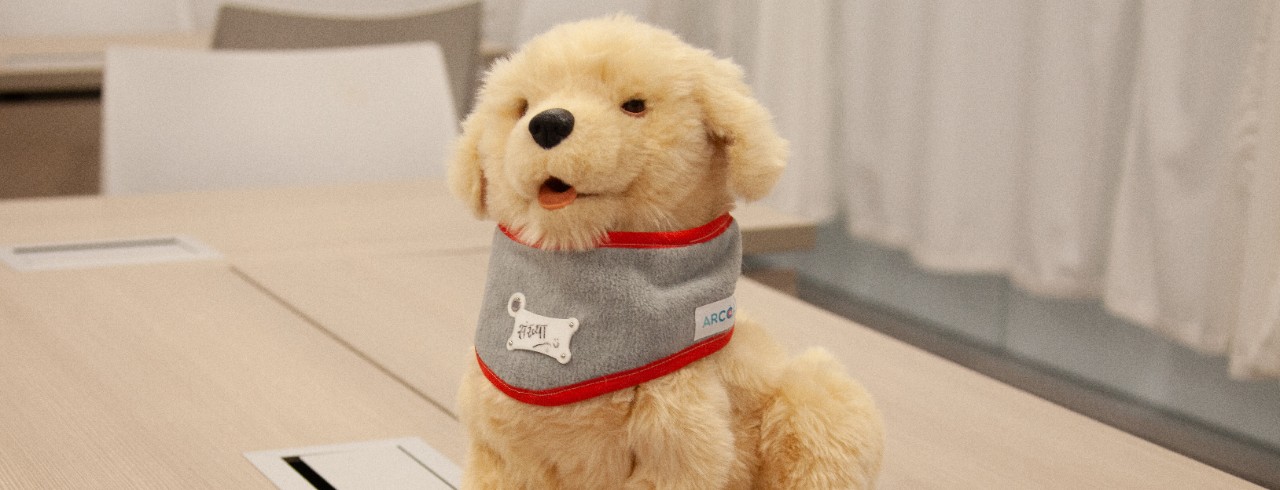 Robot golden retriever puppy sits on a table next to three tablets
