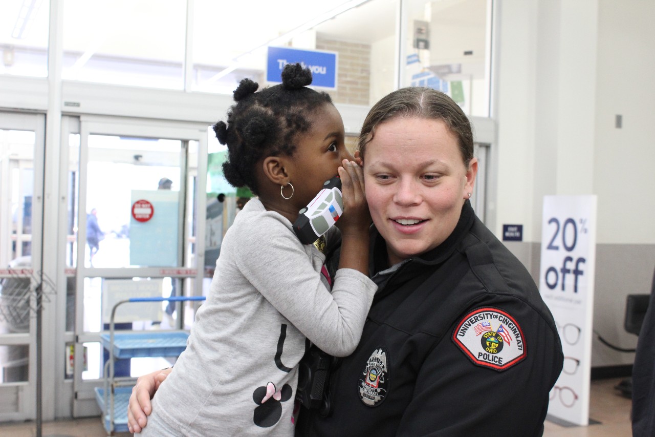 C’Zaya Johnson whispers into the ear of University of Cincinnati Police Officer Wendy Martin during the UC Police Division’s annual Shop with a Cop event on Dec. 14, 2019.