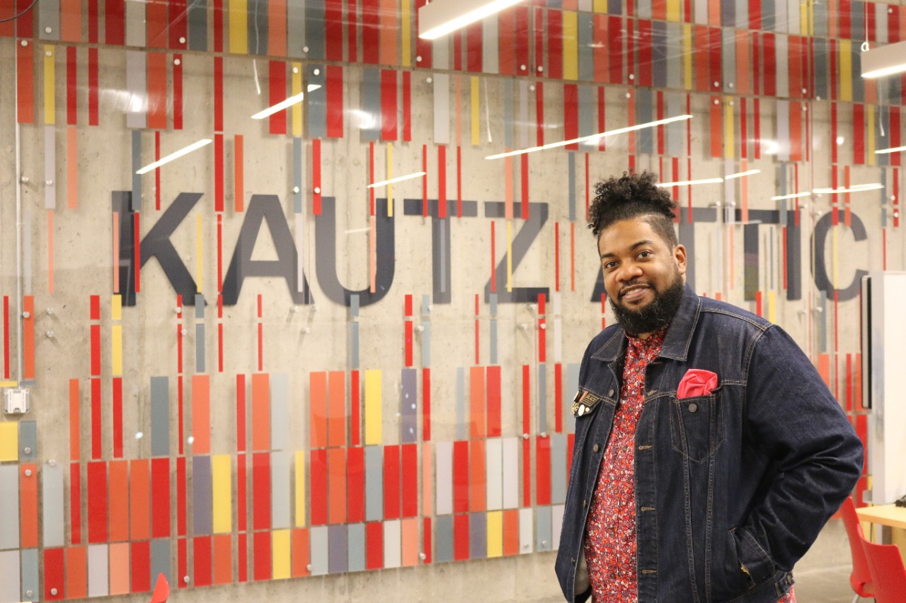 A man in a red shirt and blue jacket poses for a picture.