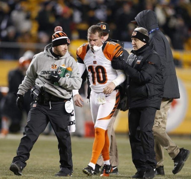 two athletic trainers help an injured football player off the field