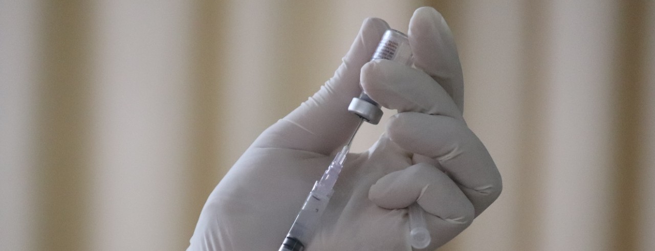 A gloved hand loads a needle with a vial of medication